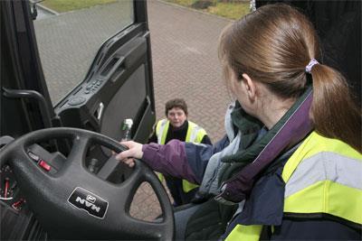 A woman driver behind at the wheel of a truck, being instructed.